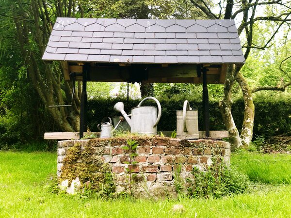 Ein gemauerter Brunnen mit Dach und mehreren Metallgießkannen auf dem Rand.